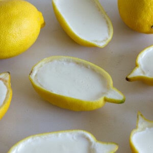 Halved lemons with the insides scooped out, filled with a creamy white dessert and placed on a light surface.
