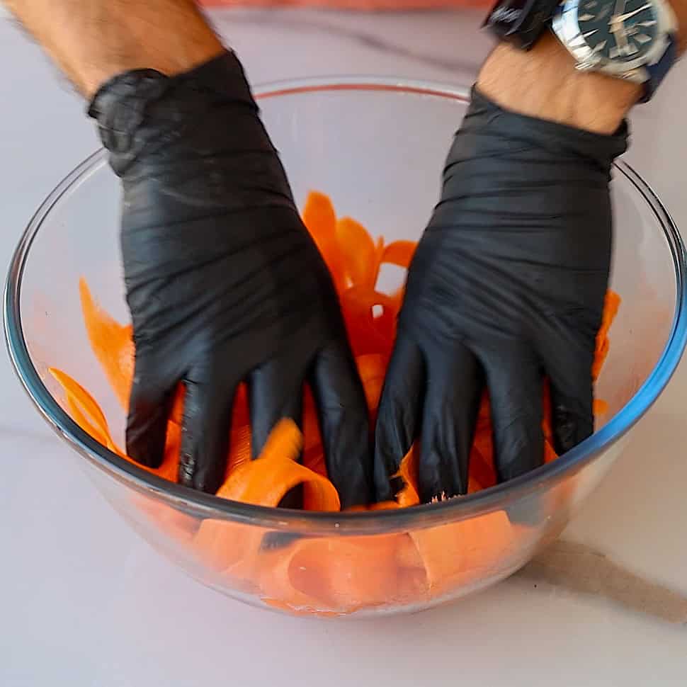 A person's hands in black gloves in a bowl of carrots.