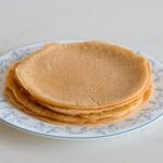 A stack of plain, round flatbread on a white plate with a blue floral pattern, set on a light-colored surface.