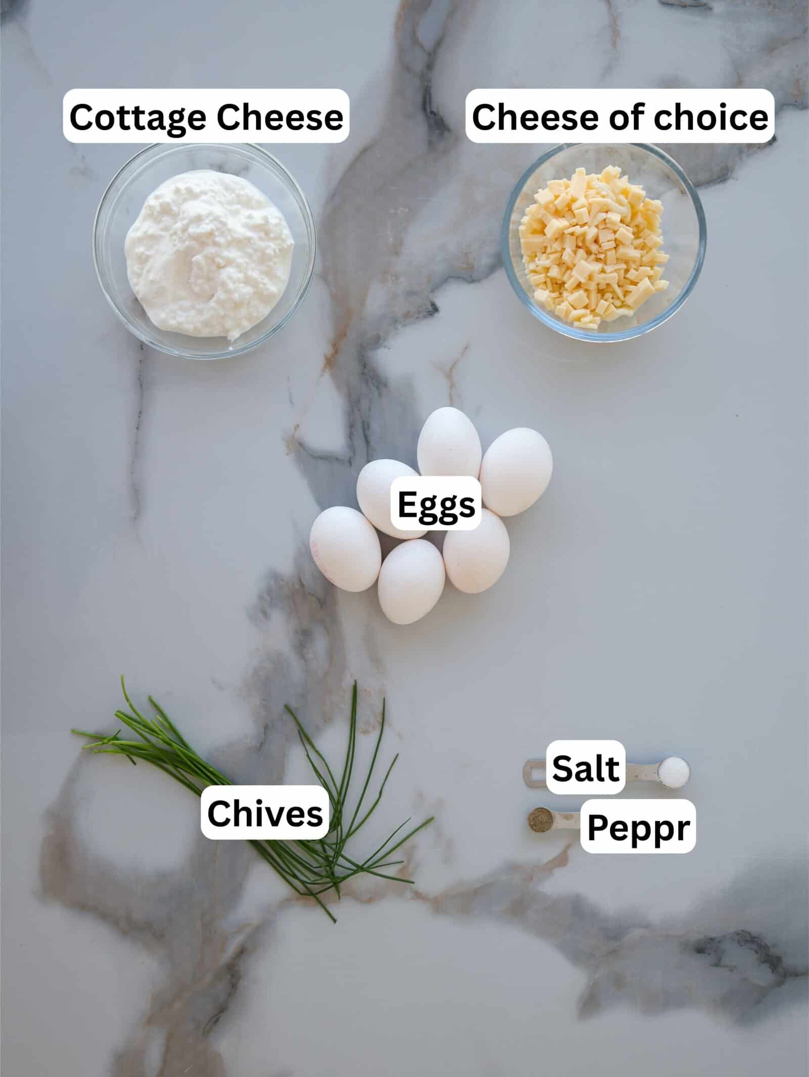 A marble surface with labeled ingredients: a bowl of cottage cheese, a bowl of shredded cheese, five eggs, fresh chives, salt, and pepper.