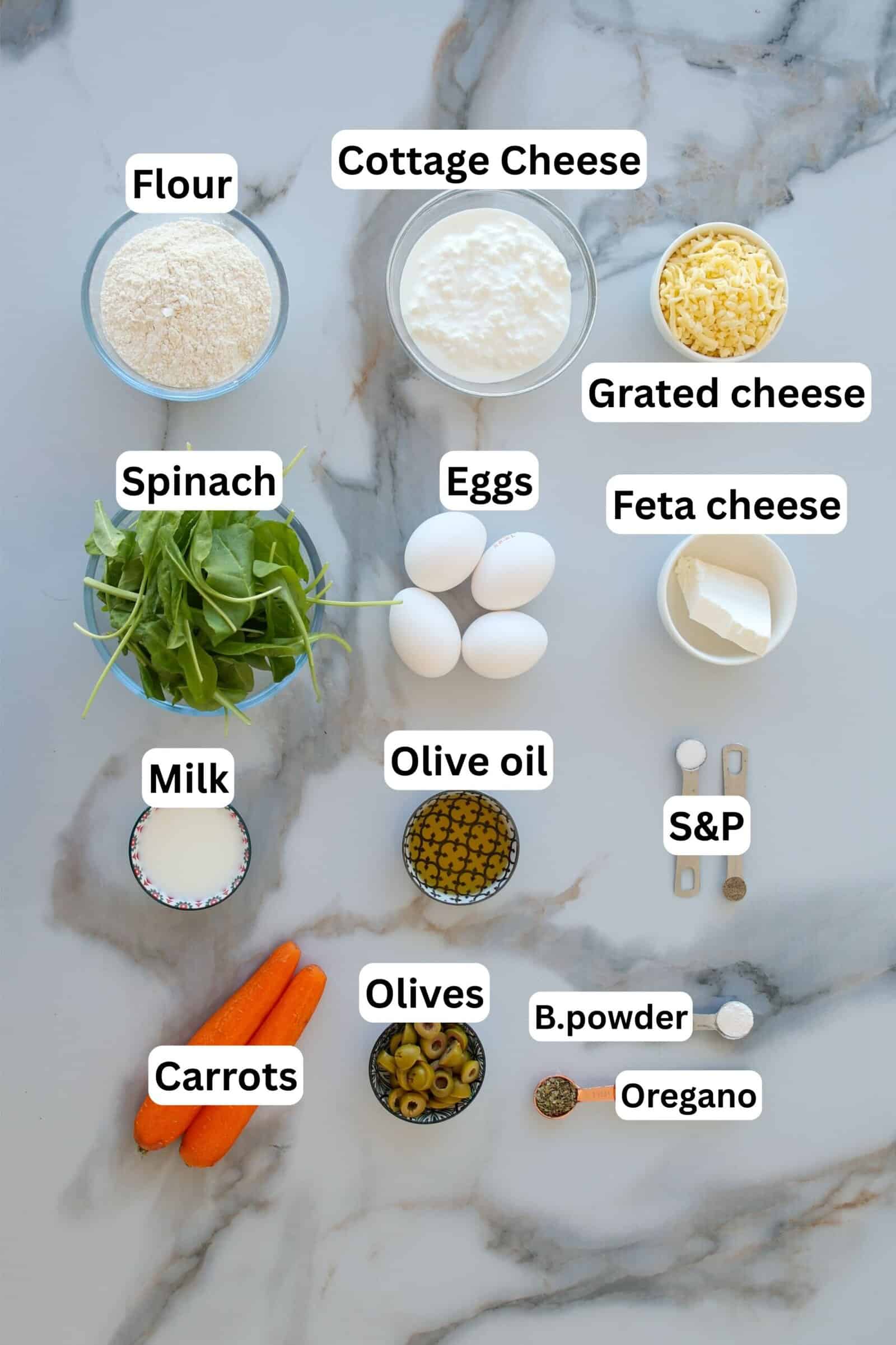 Various labeled ingredients are arranged on a marble surface, including flour, cottage cheese, grated cheese, feta cheese, spinach, eggs, milk, olive oil, olives, carrots, baking powder, oregano, salt, and pepper.