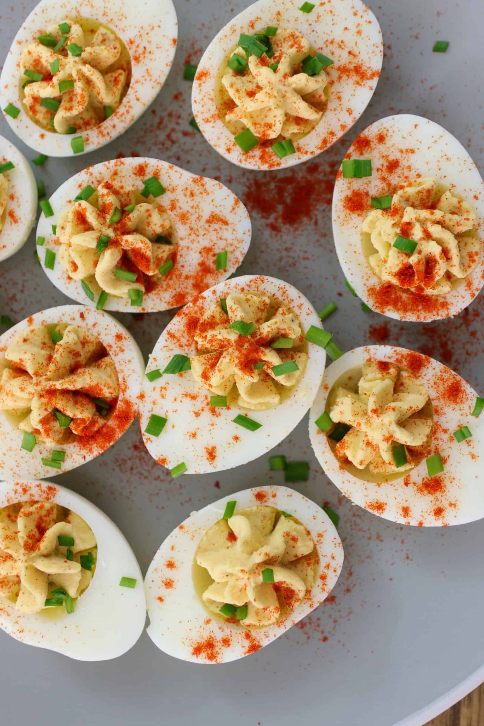 A plate of creamy deviled eggs topped with chopped chives and sprinkled with smoked paprika, arranged neatly on a light-colored surface.