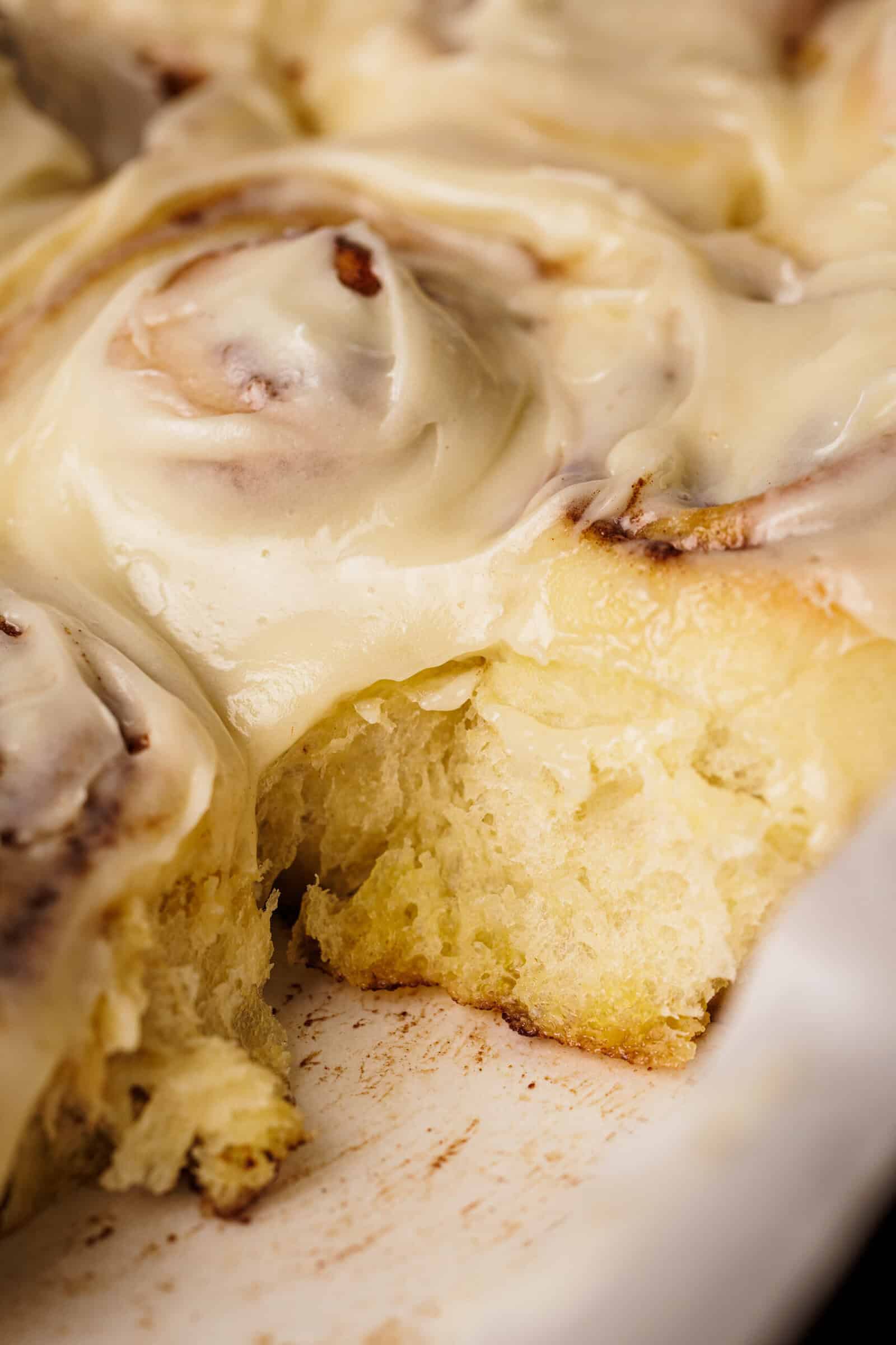 Close-up of a frosted cinnamon roll with creamy icing, showing a soft, fluffy interior where a piece has been removed.