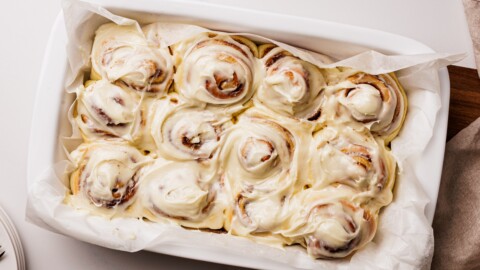 Soft Cinnamon Rolls with Cream Cheese Frosting A baking dish lined with parchment paper, filled with freshly baked cinnamon rolls topped with creamy white icing, seen from above.