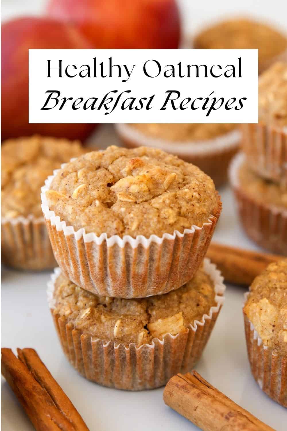 Two healthy oatmeal muffins stacked, with more muffins around. Cinnamon sticks and a peach are in the background. A label above reads: “Healthy Oatmeal Breakfast Recipes.”.