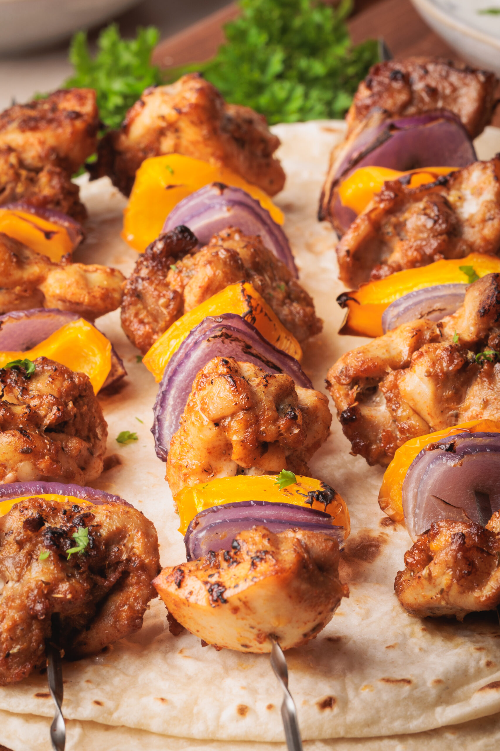 Baked chicken skewers with pieces of yellow bell pepper and red onion served on flatbread, garnished with fresh herbs.