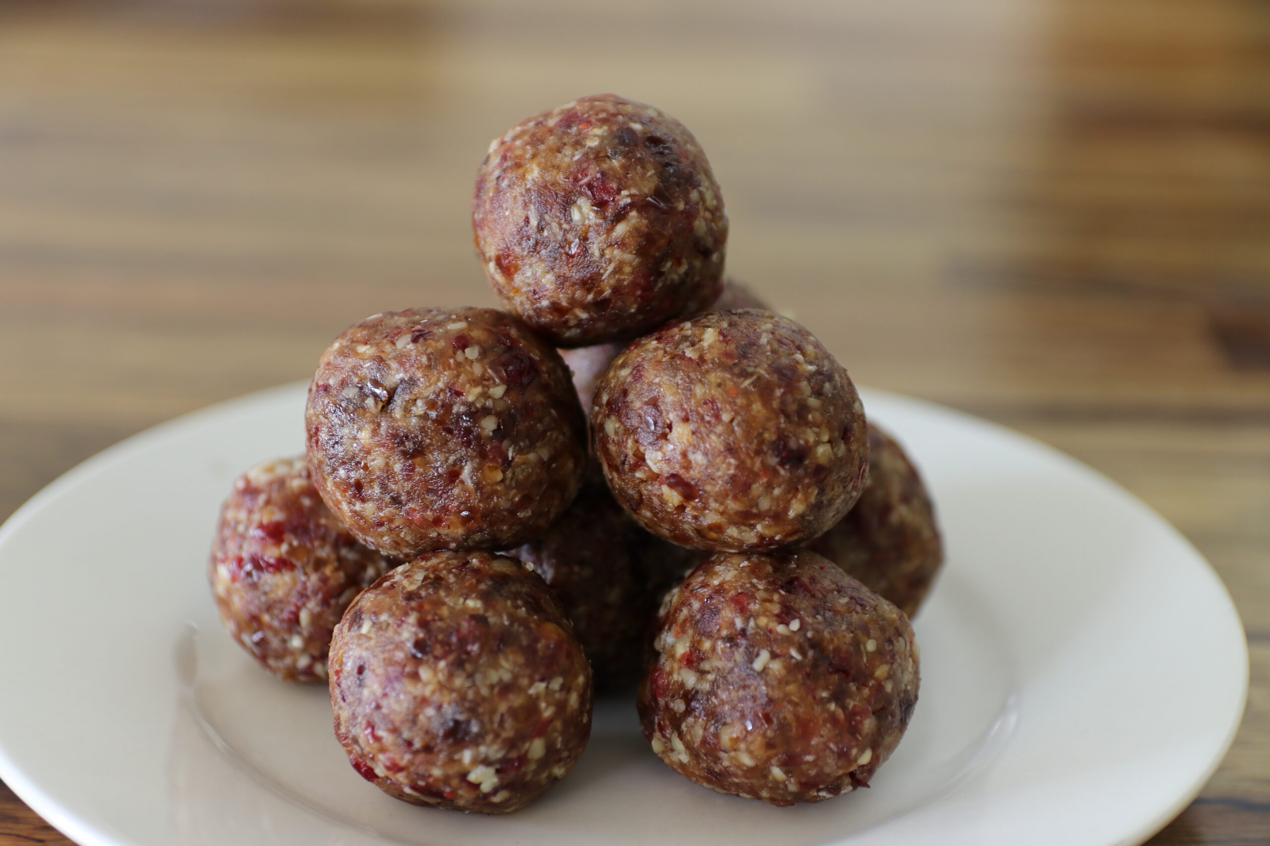 A stack of homemade date energy balls made from nuts and dried fruit sits on a white plate with a wooden table in the background.