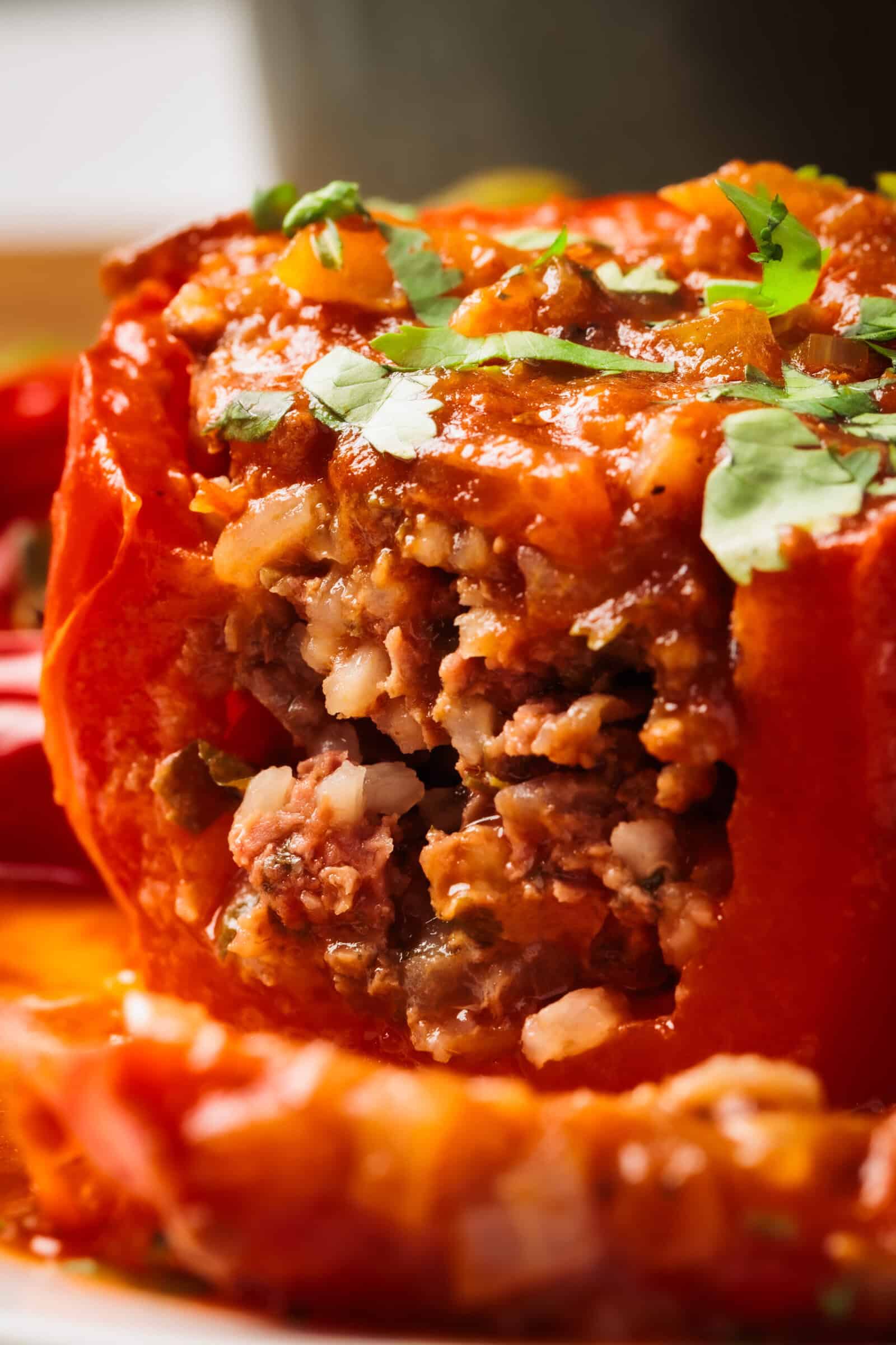 Close-up of a Mediterranean stuffed red bell pepper filled with a savory mixture of ground meat, rice, and vegetables, topped with tomato sauce and garnished with chopped fresh herbs.