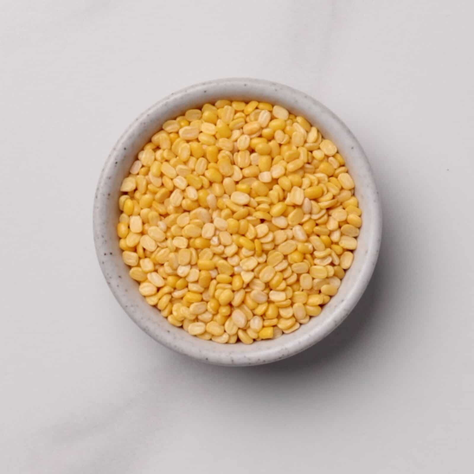 A small, round, white bowl filled with mung beans, placed on a light gray surface.