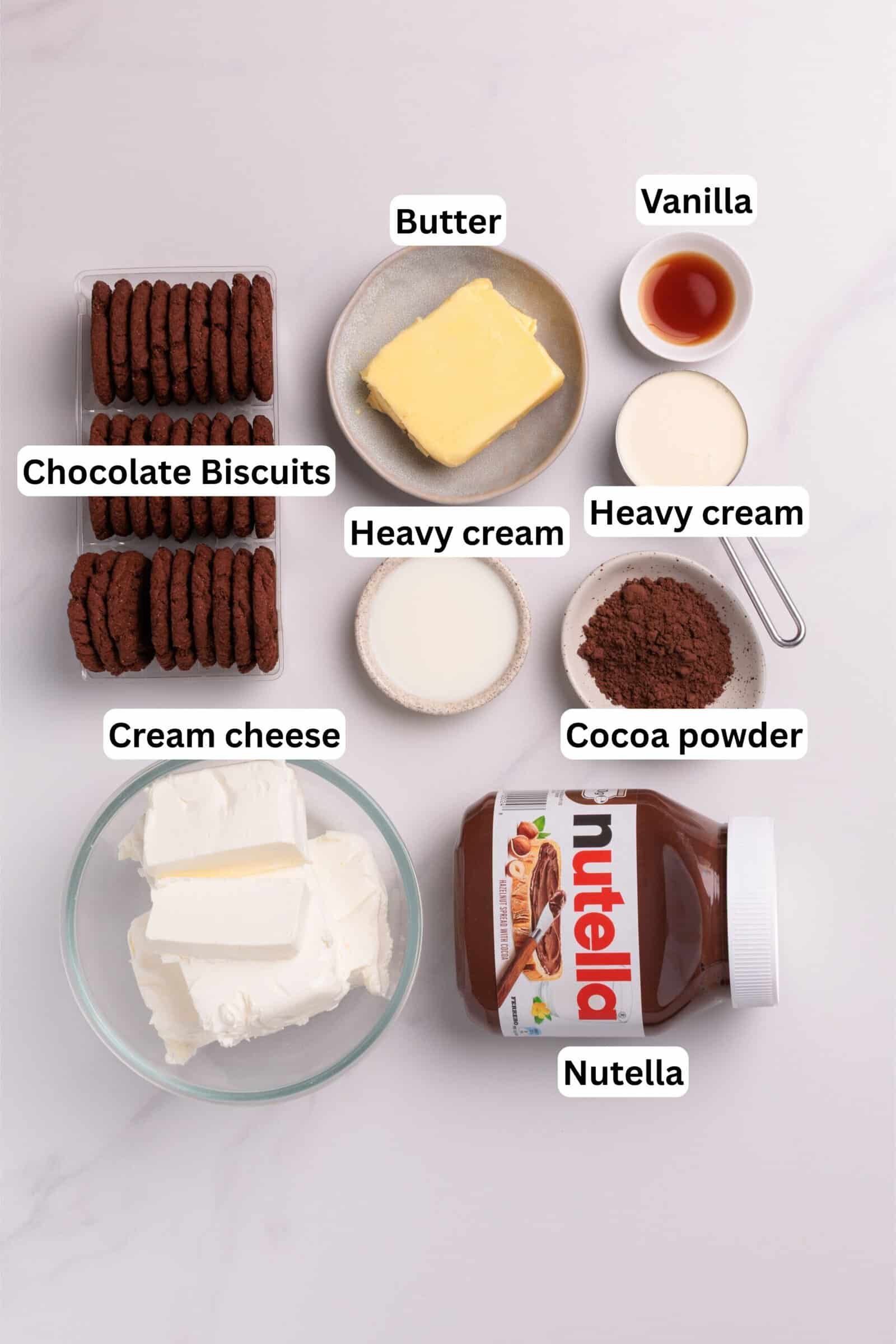 Labeled ingredients on a white surface: chocolate biscuits, butter, vanilla, heavy cream (in two portions), cocoa powder, cream cheese, and a jar of Nutella.