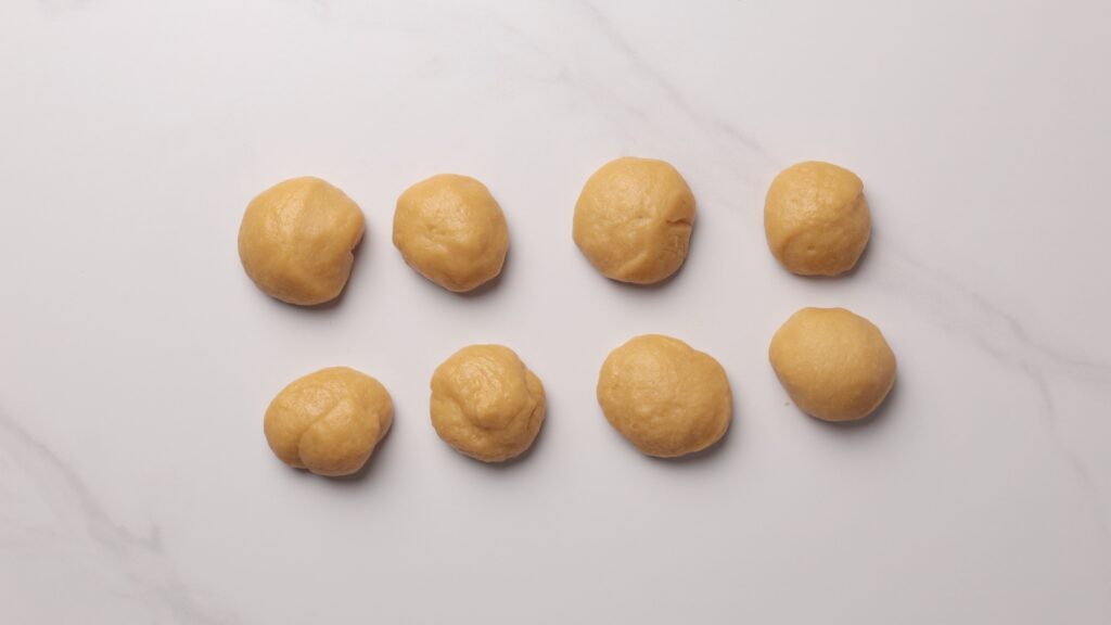 Eight evenly spaced balls of dough are arranged in two rows on a white marble surface.