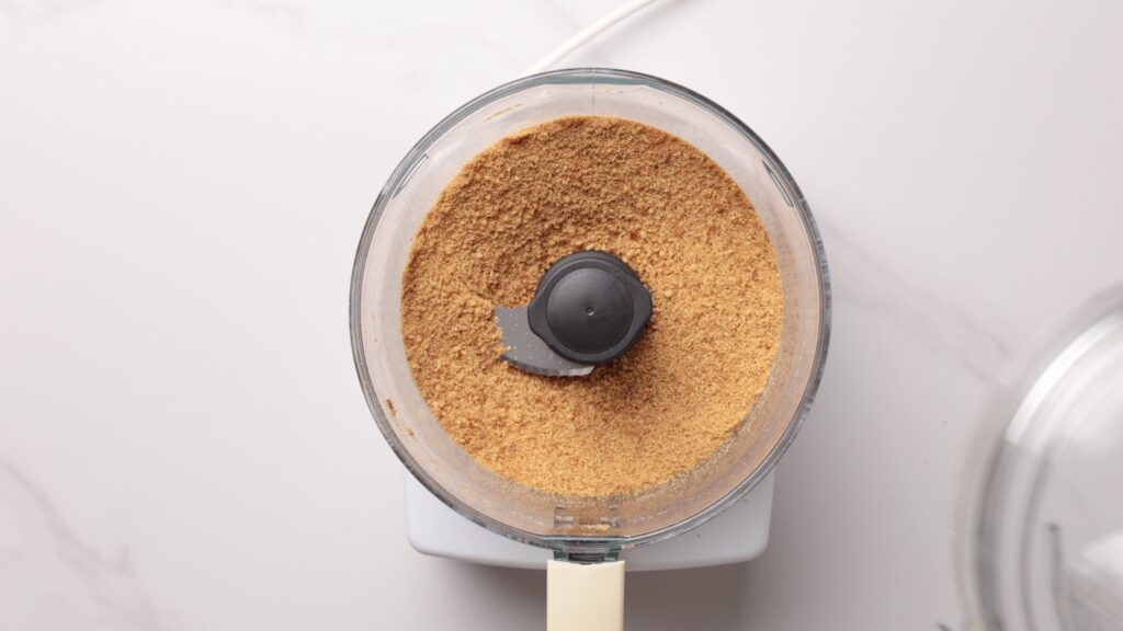 A top-down view of a food processor filled with finely ground crumbs on a white countertop.