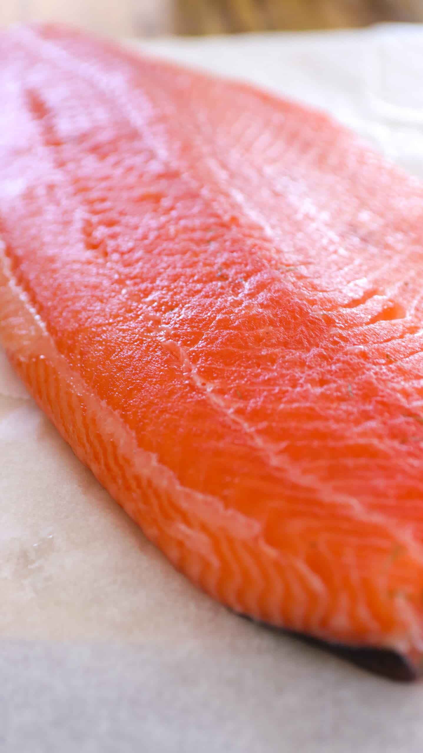 A close-up of a raw salmon fillet resting on a sheet of parchment paper, showcasing its vibrant orange color and smooth texture.