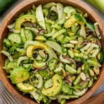 A bowl filled with fresh celery and cucumber that contains: sliced avocado, cucumber, celery, red onion, and mint leaves, topped with almond slivers and dried cranberries.