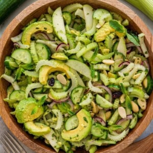 A bowl filled with fresh celery and cucumber that contains: sliced avocado, cucumber, celery, red onion, and mint leaves, topped with almond slivers and dried cranberries.