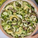 A bowl of celery cucumber salad containing sliced avocado, cucumber, fennel, apple, red onion, almonds, and fresh mint leaves, all mixed together in a light, green dressing.