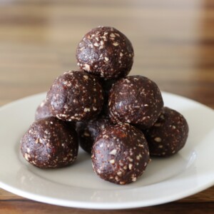 A white plate holds a pyramid stack of chocolate energy bites with dates and visible bits of nuts, set on a wooden table.