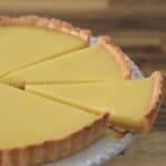 A close-up of a lemon tart with a buttery crust, sliced into pieces and displayed on a white plate, with one slice slightly separated from the rest.