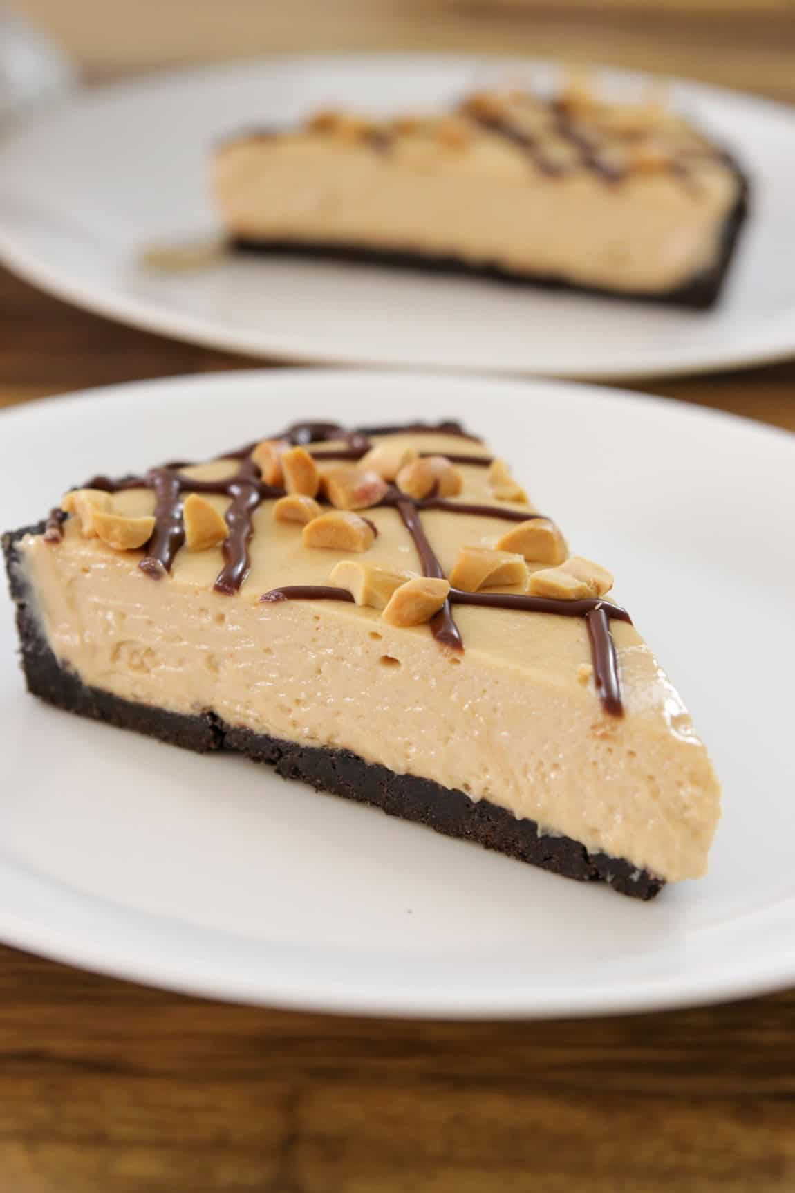 A slice of creamy peanut butter pie with a chocolate cookie crust, topped with chopped peanuts and drizzled with chocolate, served on a white plate.