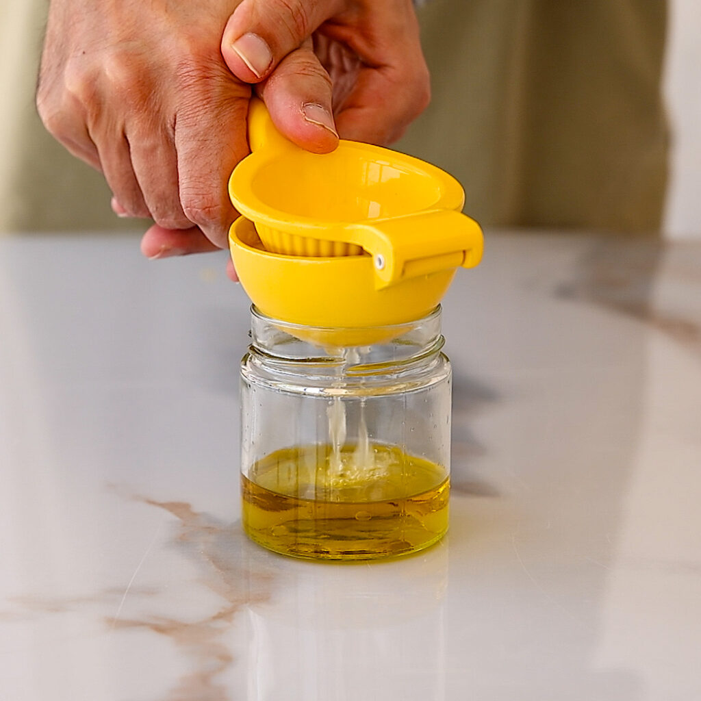 A person squeezing fresh lemon juice for a lemon mint dressing for celery cucumber salad on a white marble surface.