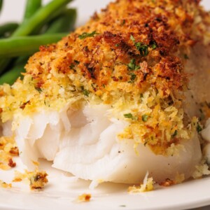 Crispy baked panko-crusted cod fillet with herbs on a white plate.