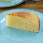 A slice of homemade sweetened condensed milk cake is served on a light blue plate. The cake has a golden brown top and a soft, moist texture.