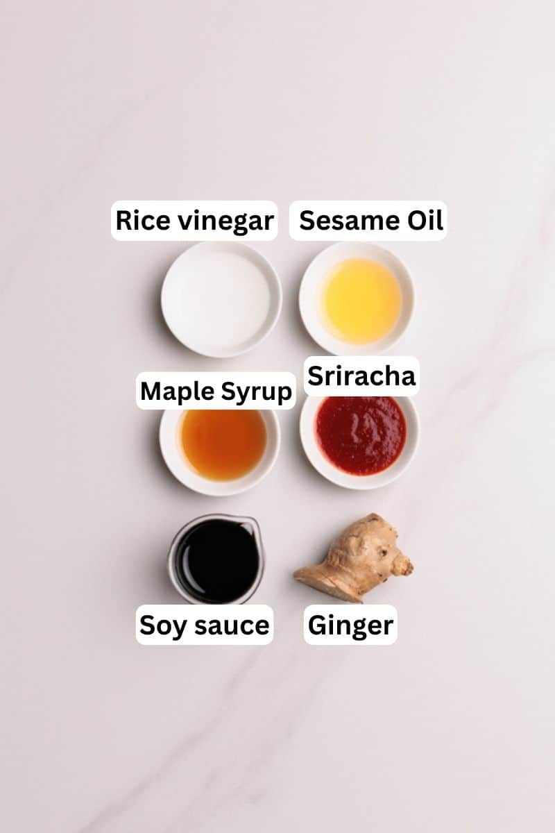 Six small bowls and a piece of ginger are arranged on a light surface, each labeled: rice vinegar, sesame oil, maple syrup, sriracha, soy sauce, and ginger.