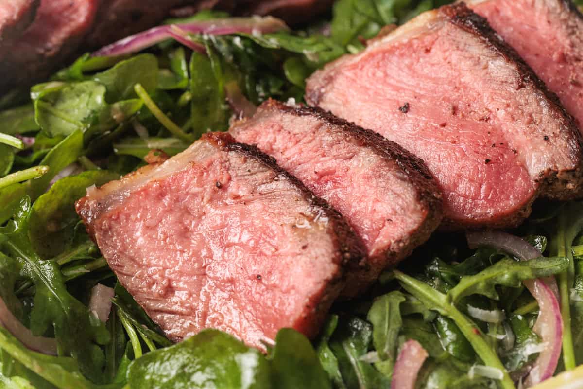 Arugula steak salad with medium-rare steak with a seared crust, served on a bed of fresh arugula and thinly sliced red onions.