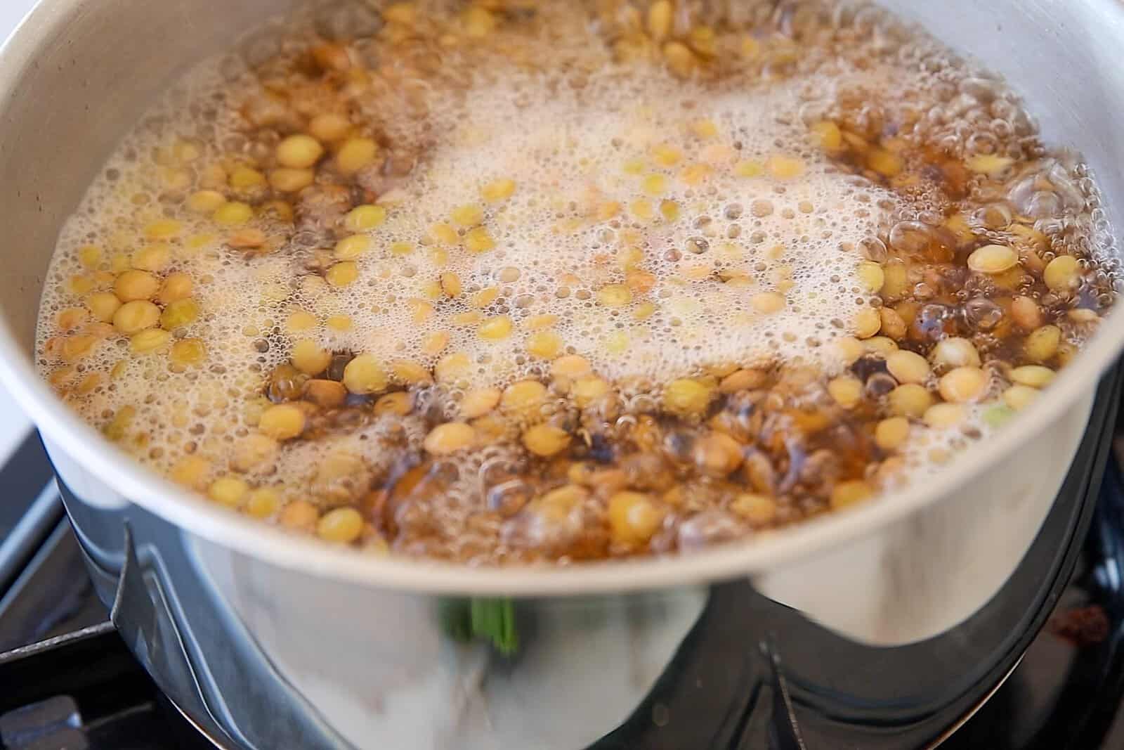 A pot of lentils boiling on a stove, with foam and bubbles forming on the surface of the water.