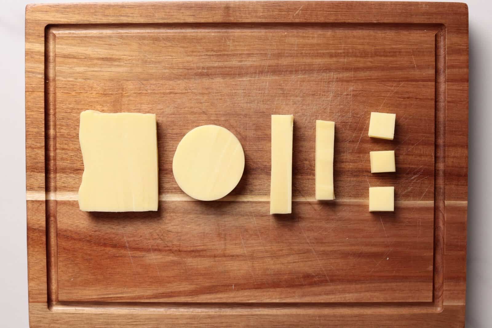 Various mozzarella cheese pieces in different shapes—rectangle, oval, sticks, and cubes—are neatly arranged on a wooden cutting board.