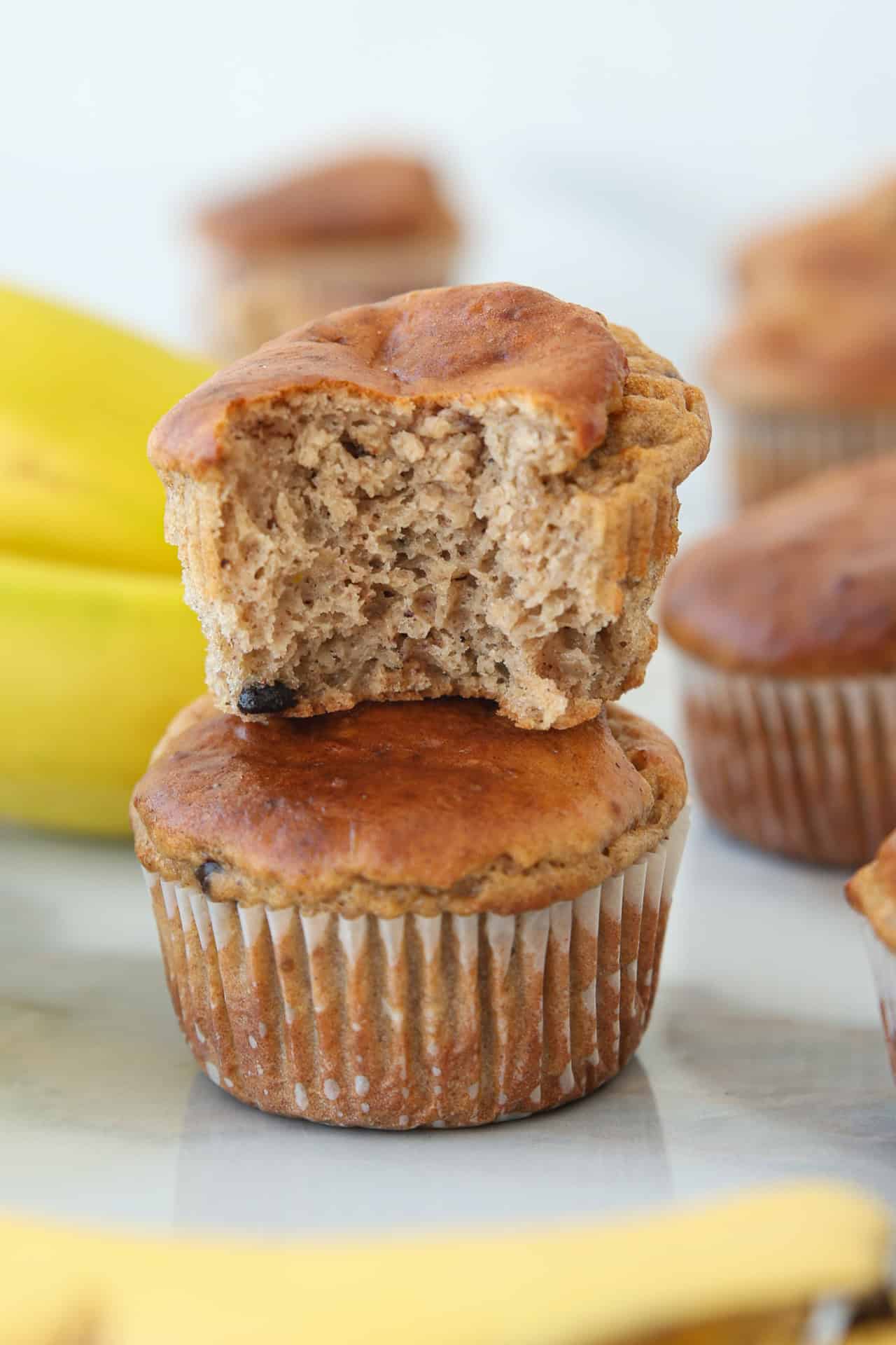 A bitten cottage cheese banana muffin sits atop a whole muffin, with bananas and more muffins in the blurred background.