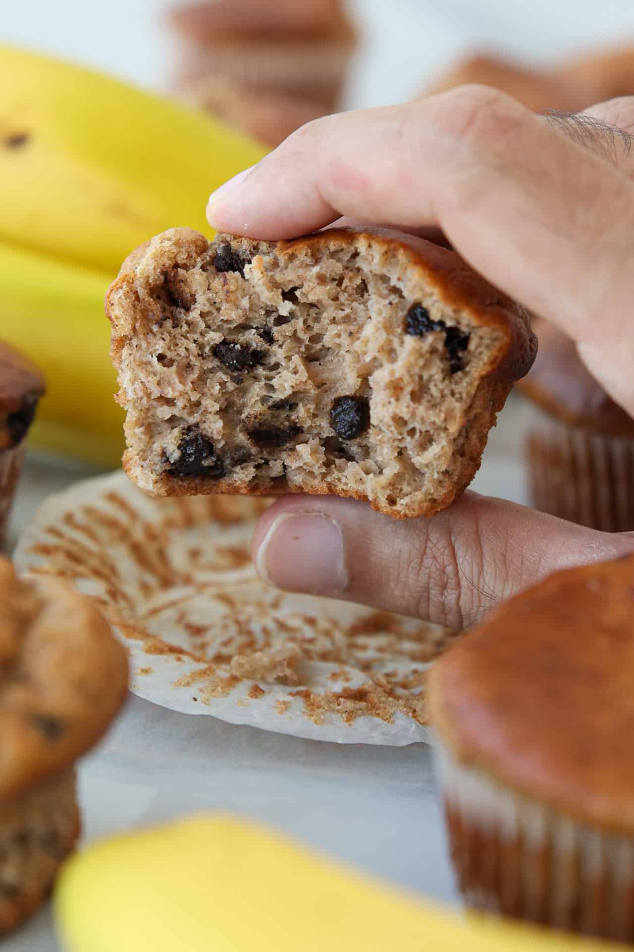 A hand holds a half-eaten banana cottage cheese muffin, revealing its soft and moist interior.
