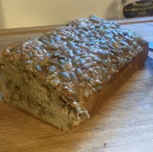 Loaf of bread topped with pumpkin and sunflower seeds on a wooden cutting board.