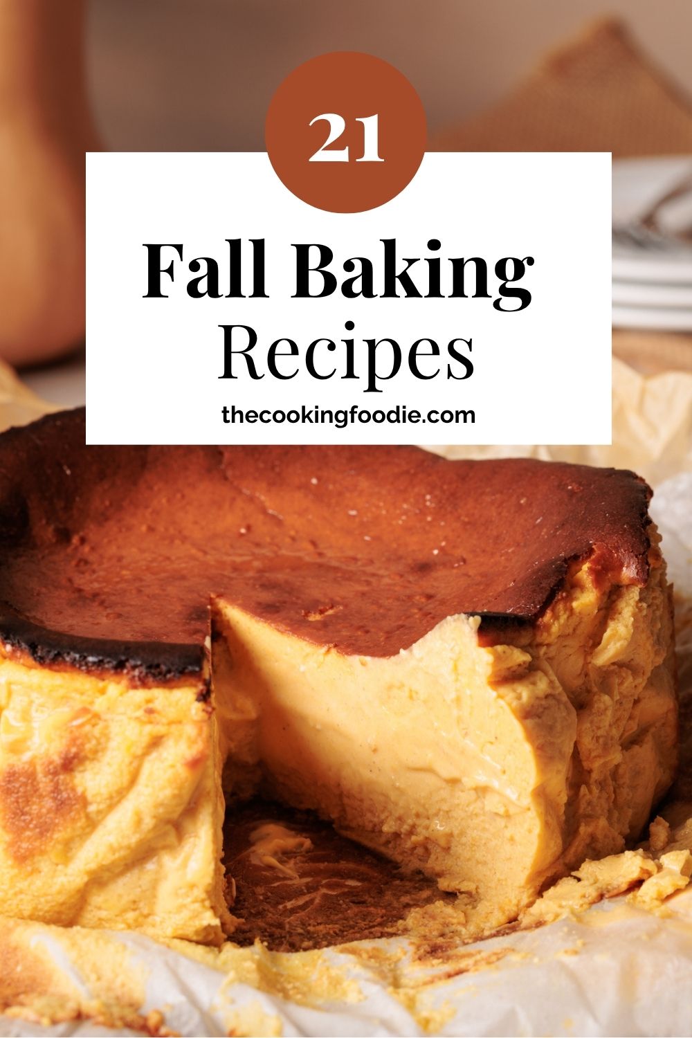 A pumpkin cheesecake with a slice removed sits on parchment paper. Text on the image reads: “21 Fall Baking Recipes thecookingfoodie.com.”.