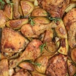 Easy one-pan roasted chicken drumsticks and thighs with golden potato wedges, onion slices, and sprigs of rosemary, all baked and seasoned, arranged closely together.