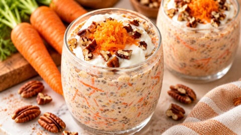 Carrot Cake Overnight Oats Two glass jars of carrot cake overnight oats topped with yogurt, shredded carrots, and pecans, with whole carrots and scattered pecans nearby.
