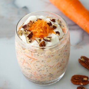 A glass jar of carrot cake overnight oats topped with yogurt, shredded carrots, and pecans.